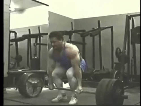 A Man Is Lifting A Barbell In A Gym In Front Of A Mirror . GIF