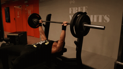 A Man Is Lifting A Barbell On A Bench In Front Of A Sign That Says Free Yachts GIF