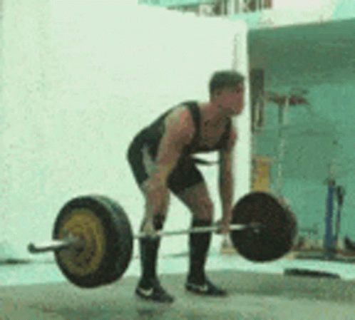 A Man Is Lifting A Barbell On A Concrete Surface . GIF