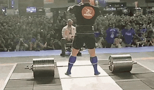 A Man Is Lifting A Barbell On A Stage In Front Of A Crowd Of People . GIF