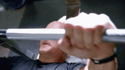A Man Is Lifting A Barbell While Sitting On A Bench In A Gym . GIF