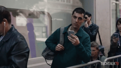 A Man Is Looking At His Phone In Front Of A Sign That Says Tech Talk Tv GIF
