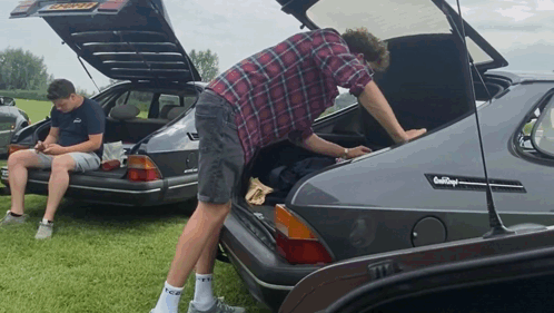 A Man Is Looking Into The Trunk Of A Car That Says Saab Royal GIF