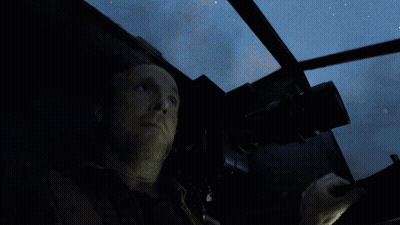 A Man Is Looking Out A Window With A Blue Light Behind Him GIF