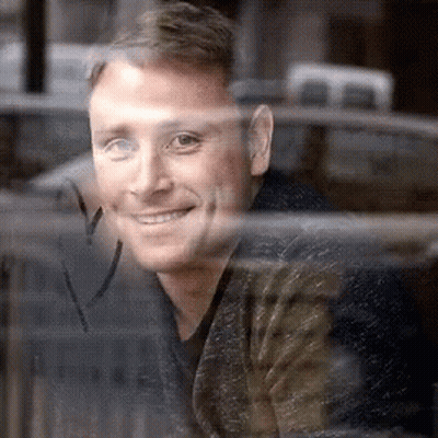 A Man Is Looking Out Of A Window And Smiling . GIF