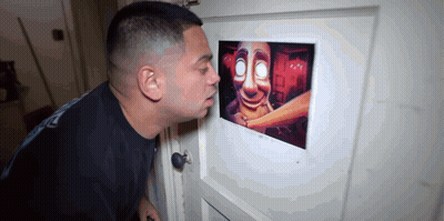 A Man Is Looking Through A Peephole At A Picture Of A Scary Face . GIF