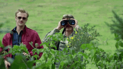 A Man Is Looking Through Binoculars In A Field While Another Man Looks On . GIF