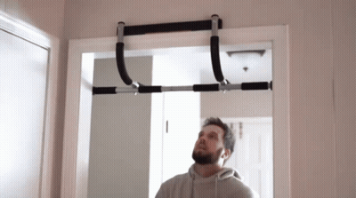 A Man Is Looking Up At A Pull Up Bar Hanging From A Doorway . GIF