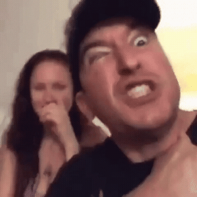 A Man Is Making A Funny Face While A Woman Laughs In The Background . GIF