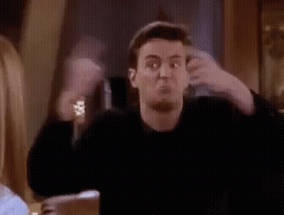 A Man Is Making A Funny Face While Sitting At A Table With His Arms Outstretched In A Room . GIF