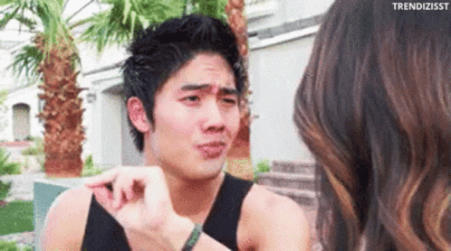 A Man Is Making A Funny Face While Talking To A Woman In Front Of A Palm Tree . GIF