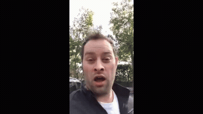 A Man Is Making A Funny Face While Wearing A Black Jacket And A White Shirt . GIF