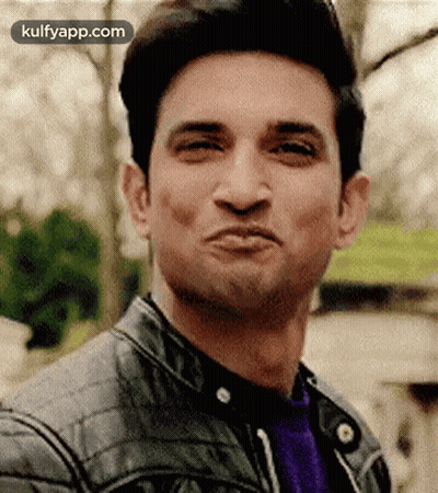 A Man Is Making A Funny Face While Wearing A Leather Jacket And A Purple Shirt . GIF