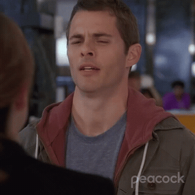 A Man Is Making A Funny Face With His Eyes Closed While Talking To A Woman . GIF