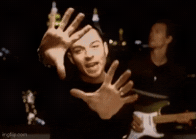 A Man Is Making A Funny Face With His Hands While Playing A Guitar In A Band . GIF