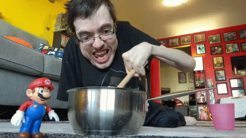 A Man Is Mixing Something In A Bowl With A Mario Toy In The Foreground GIF