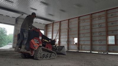 A Man Is Operating A Ditch Witch Tractor In A Garage GIF