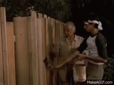 A Man Is Painting A Wooden Fence With A Brush . GIF