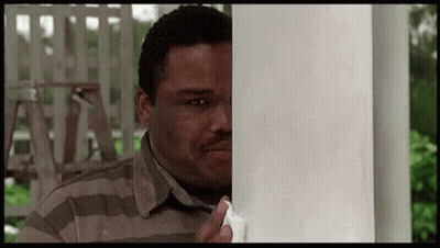 A Man Is Peeking Out From Behind A White Pole And Holding A Piece Of Paper . GIF