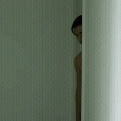 A Man Is Peeking Out Of A Doorway In A Dark Room . GIF