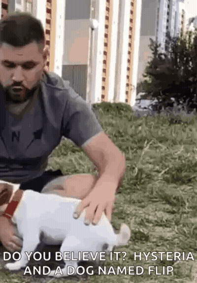 A Man Is Petting A Small White Dog In A Field . GIF