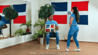 A Man Is Playing A Drum While A Woman Is Dancing In A Room With Flags Behind Them GIF