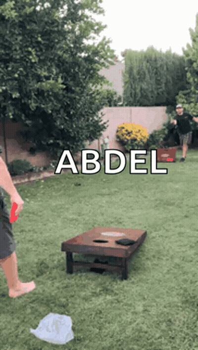 A Man Is Playing A Game Of Cornhole In A Backyard With The Name Abdel On The Bottom GIF
