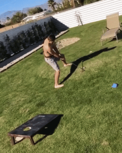 A Man Is Playing A Game Of Cornhole In The Backyard GIF