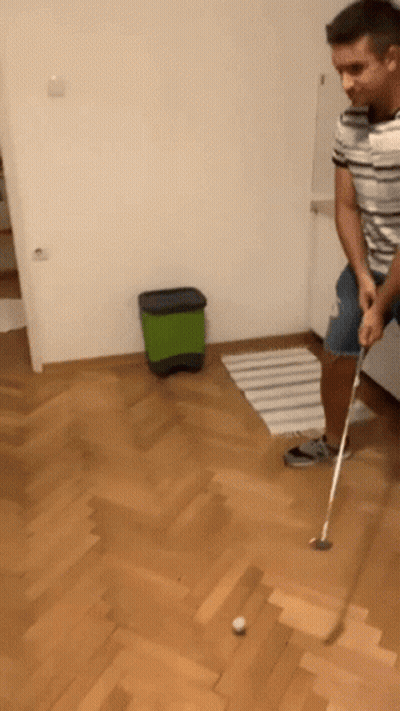 A Man Is Playing A Game Of Golf On A Hardwood Floor GIF