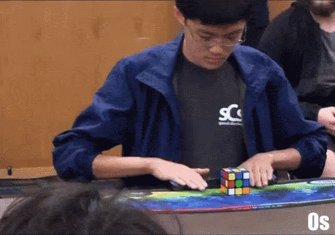 A Man Is Playing A Game Of Rubik 'S Cube While Wearing A Scs Shirt GIF