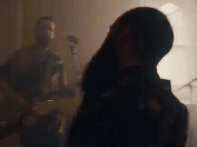 A Man Is Playing A Guitar And A Woman Is Singing Into A Microphone In A Room . GIF