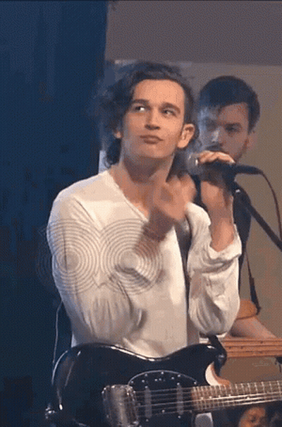 A Man Is Playing A Guitar And Singing Into A Microphone . GIF