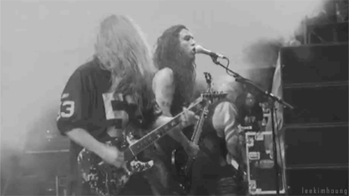 A Man Is Playing A Guitar And Singing Into A Microphone While Another Man Plays Drums . GIF