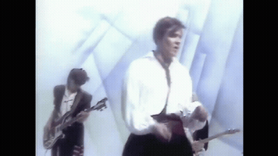A Man Is Playing A Guitar In A Band While Another Man Sings . GIF