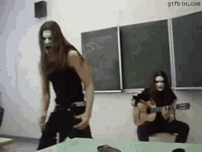A Man Is Playing A Guitar In A Classroom And A Woman Is Dancing . GIF