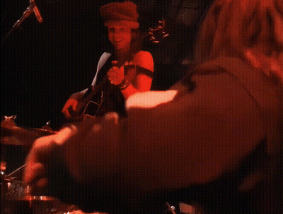 A Man Is Playing A Guitar In A Dark Room While A Woman Plays Drums . GIF