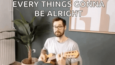 A Man Is Playing A Guitar In A Living Room With A Potted Plant . GIF