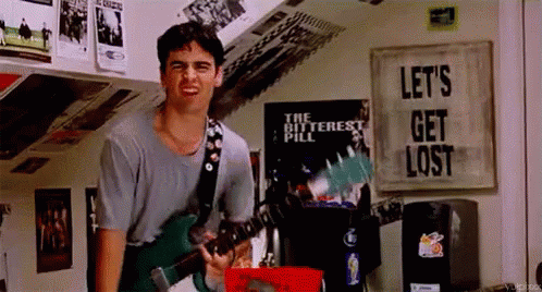 A Man Is Playing A Guitar In A Room With A Poster That Says Let 'S Get Lost . GIF