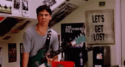 A Man Is Playing A Guitar In A Room With A Sign That Says Let 'S Get Lost GIF