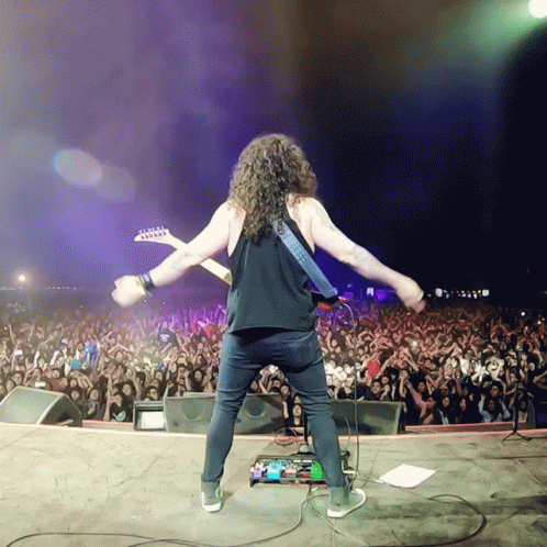 A Man Is Playing A Guitar In Front Of A Crowd GIF