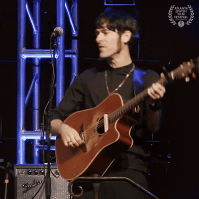 A Man Is Playing A Guitar In Front Of A Microphone With A Laurel Wreath On It GIF