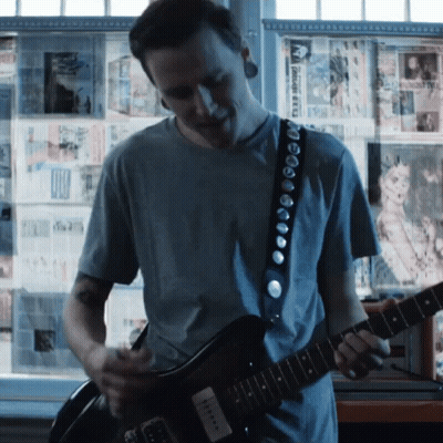 A Man Is Playing A Guitar In Front Of A Wall That Has A Picture Of A Cat GIF