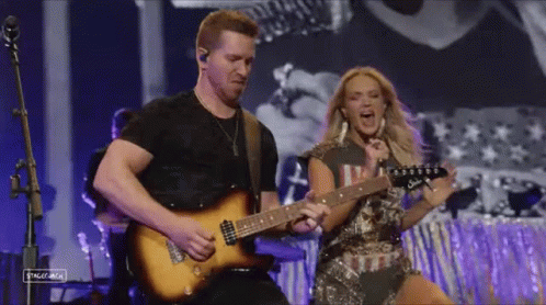 A Man Is Playing A Guitar Next To A Woman Who Is Singing Into A Microphone . GIF