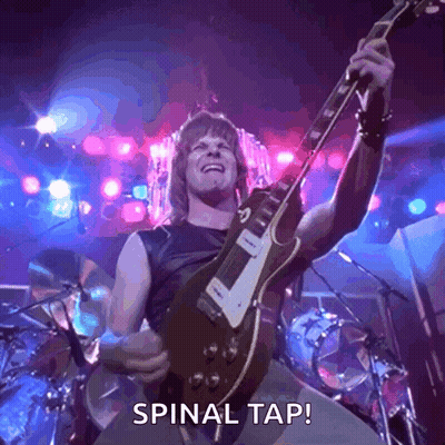 A Man Is Playing A Guitar On A Stage And The Words Spinal Tap Are On The Screen . GIF