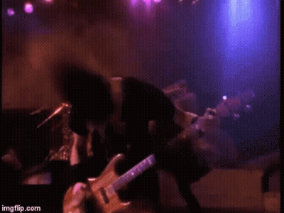 A Man Is Playing A Guitar On A Stage In A Dark Room . GIF