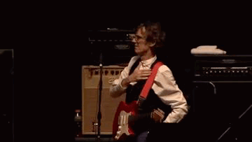 A Man Is Playing A Guitar On A Stage In Front Of An Orange Amplifier . GIF