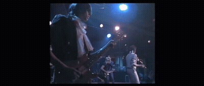 A Man Is Playing A Guitar On A Stage While Another Man Sings Into A Microphone . GIF