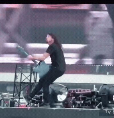 A Man Is Playing A Guitar On A Stage While Standing On A Stool . GIF