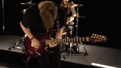 A Man Is Playing A Guitar On A Stage With A Drummer In The Background GIF