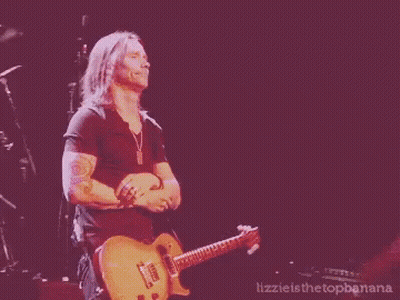 A Man Is Playing A Guitar On A Stage With The Words Lizzie Is The Topbanana Below Him GIF